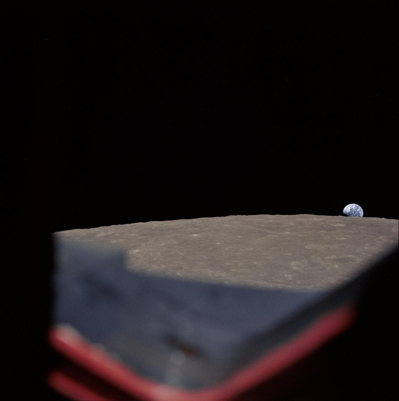 High-oblique view of Moon's surface showing earth rising above horizon
