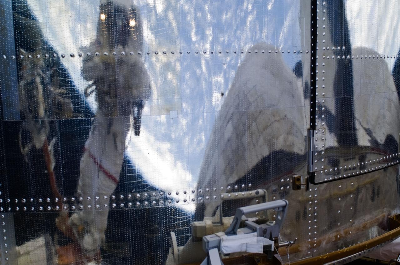 An STS-125 Crew Member's image is reflected in the HST